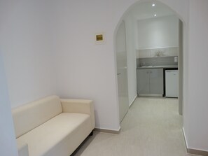 A modern interior with a sofa, a kitchen area, and a doorway leading to another room. - Makis Louvlis Luxury Apartments (Corfu)