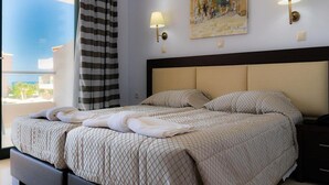Une chambre d’hôtel avec un grand lit, deux lampes de chevet, un tableau au mur et une vue sur les immeubles par la fenêtre.
