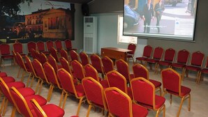Une salle de conférence avec des rangées de chaises rouges, un écran de projection et une table en bois.