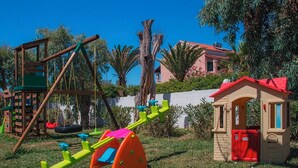 Une aire de jeux avec des balançoires, une bascule et une petite maison de jeu rouge.