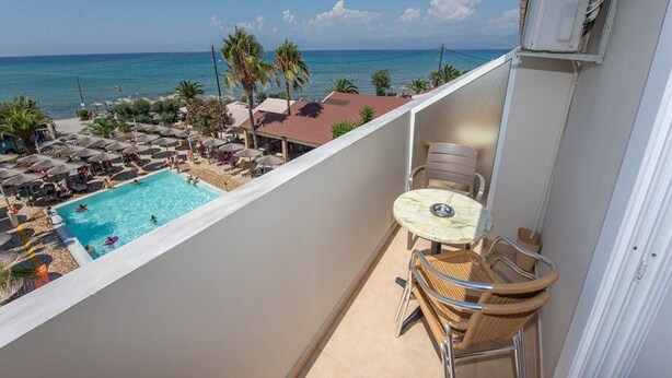 Un balcon avec une piscine, des chaises et une table, offrant une vue sur une plage et l’océan.