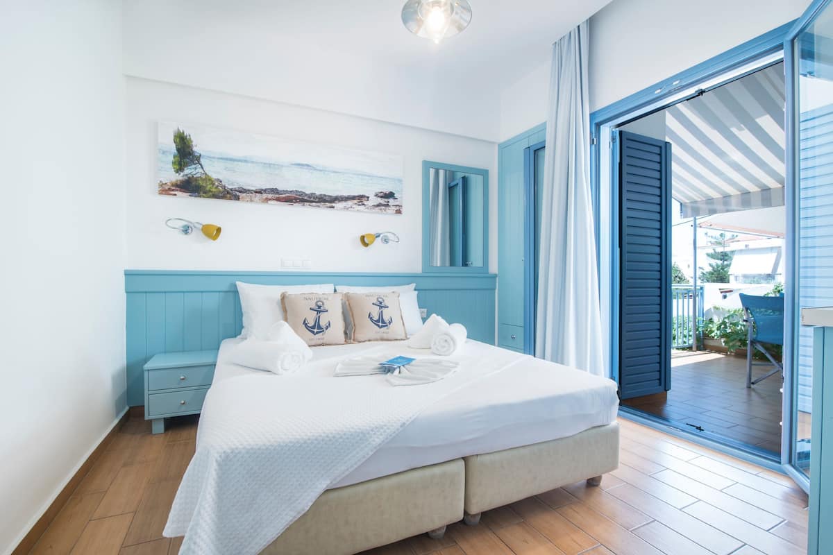 A bedroom with a bed, a nightstand, a painting, and a view of the outdoors.
