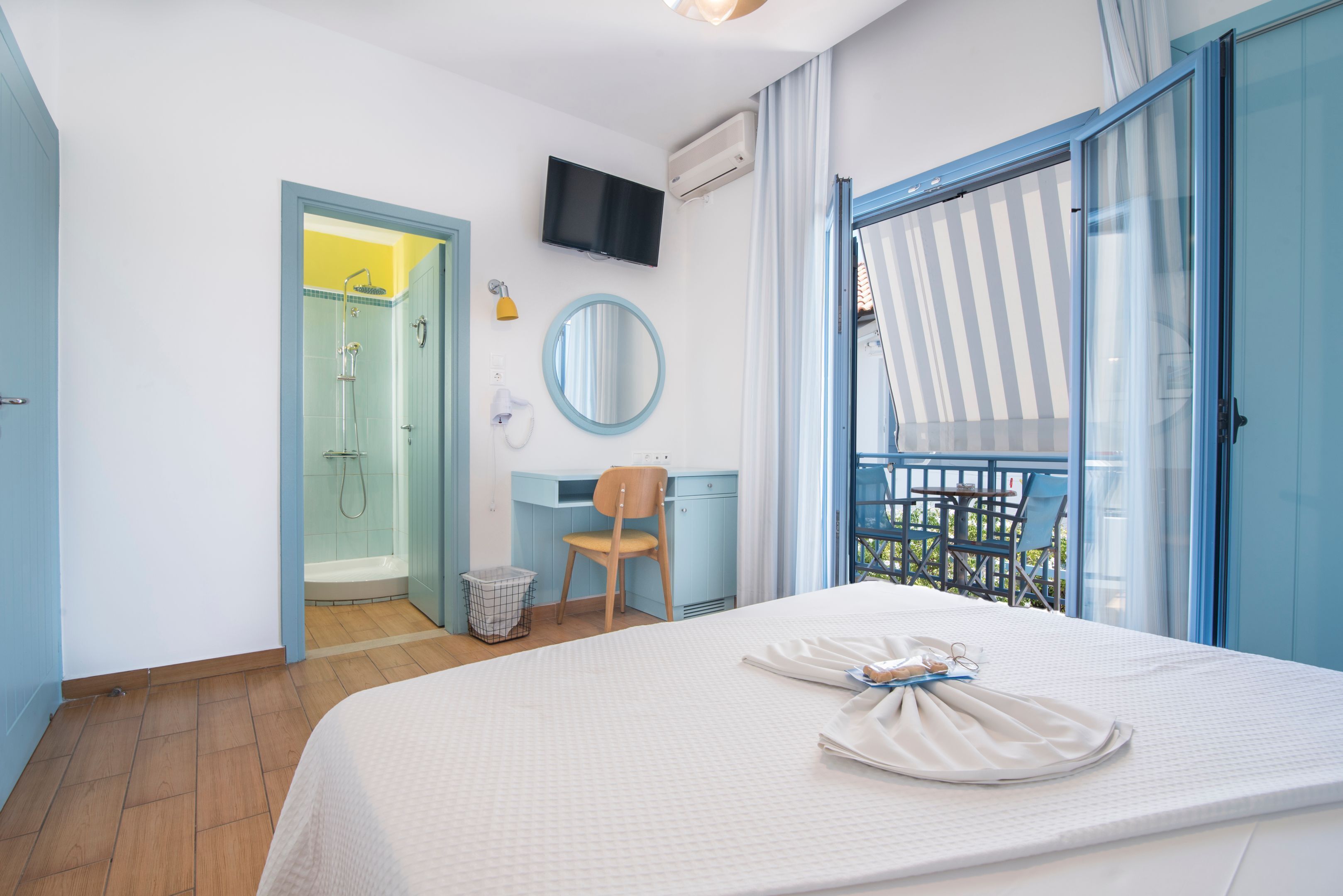 Een hotelkamer met een bed, een bureau, een stoel, een televisie, een douche en een balkon met uitzicht.