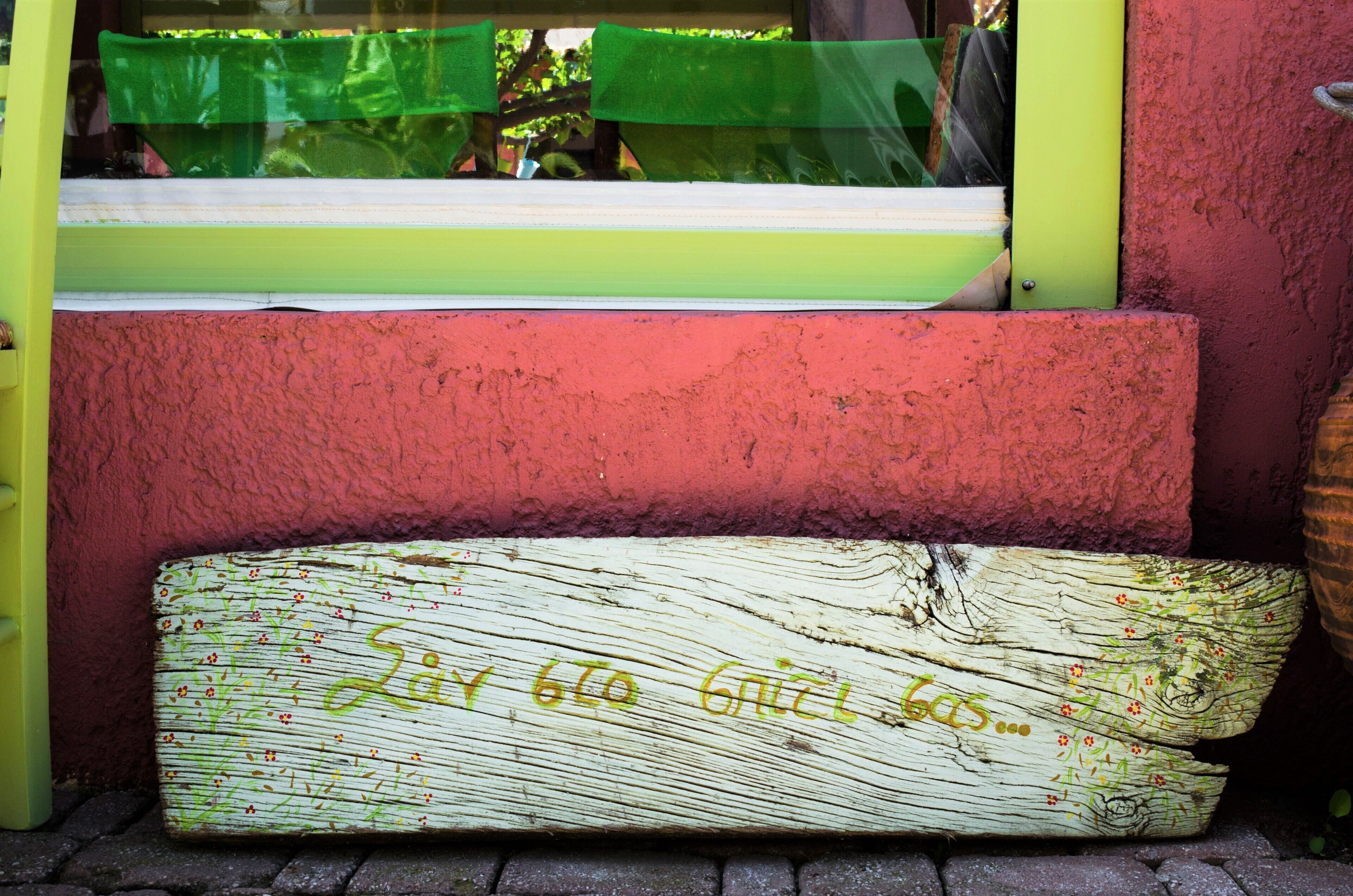 A wooden bench with graffiti, a green window, and a red wall.