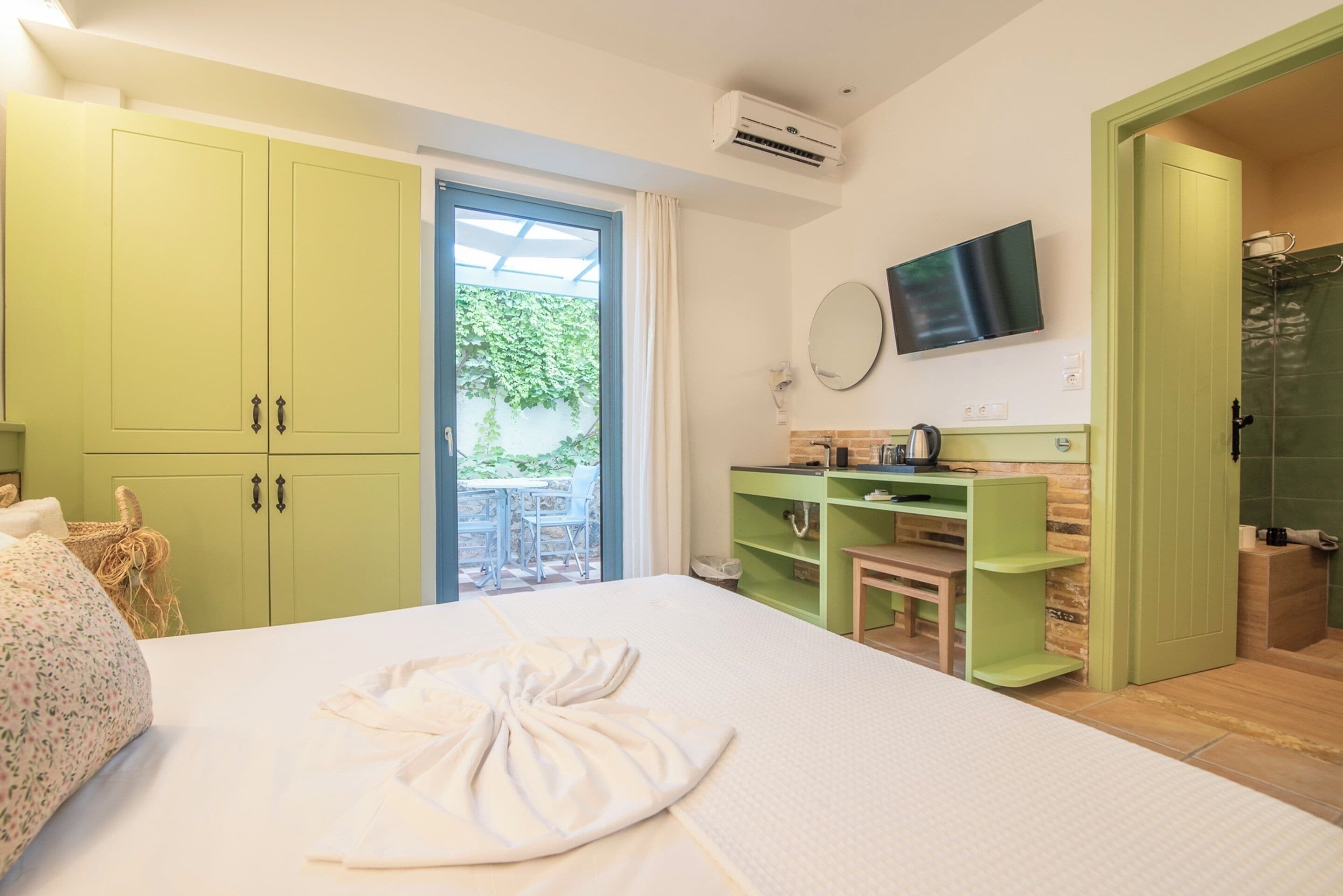 A hotel room with a bed, a TV, a green wardrobe, and a bathroom with a shower.
