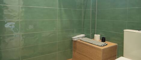 Ein Badezimmer mit grünen Fliesen, einer Holz-Dusche, einer Toilette und einem Fenster.