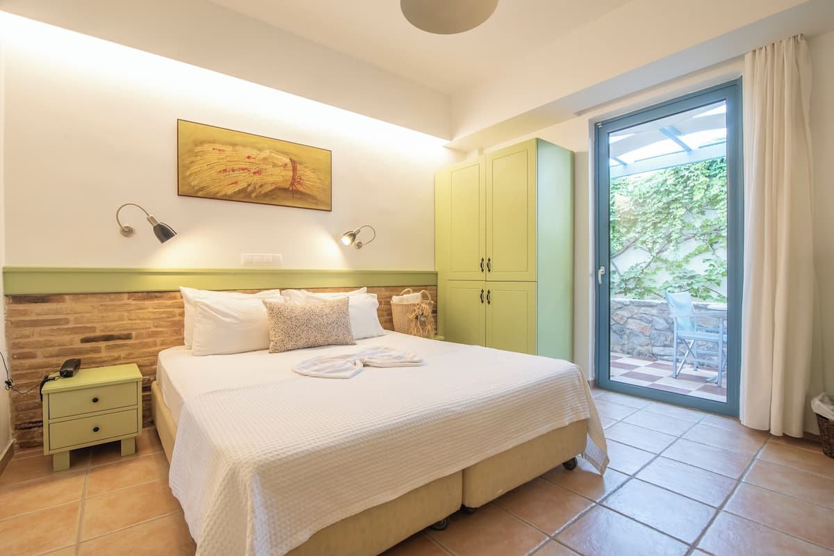 A bedroom with a large bed, a green wardrobe, a nightstand, and a view of the outdoors through a glass door.