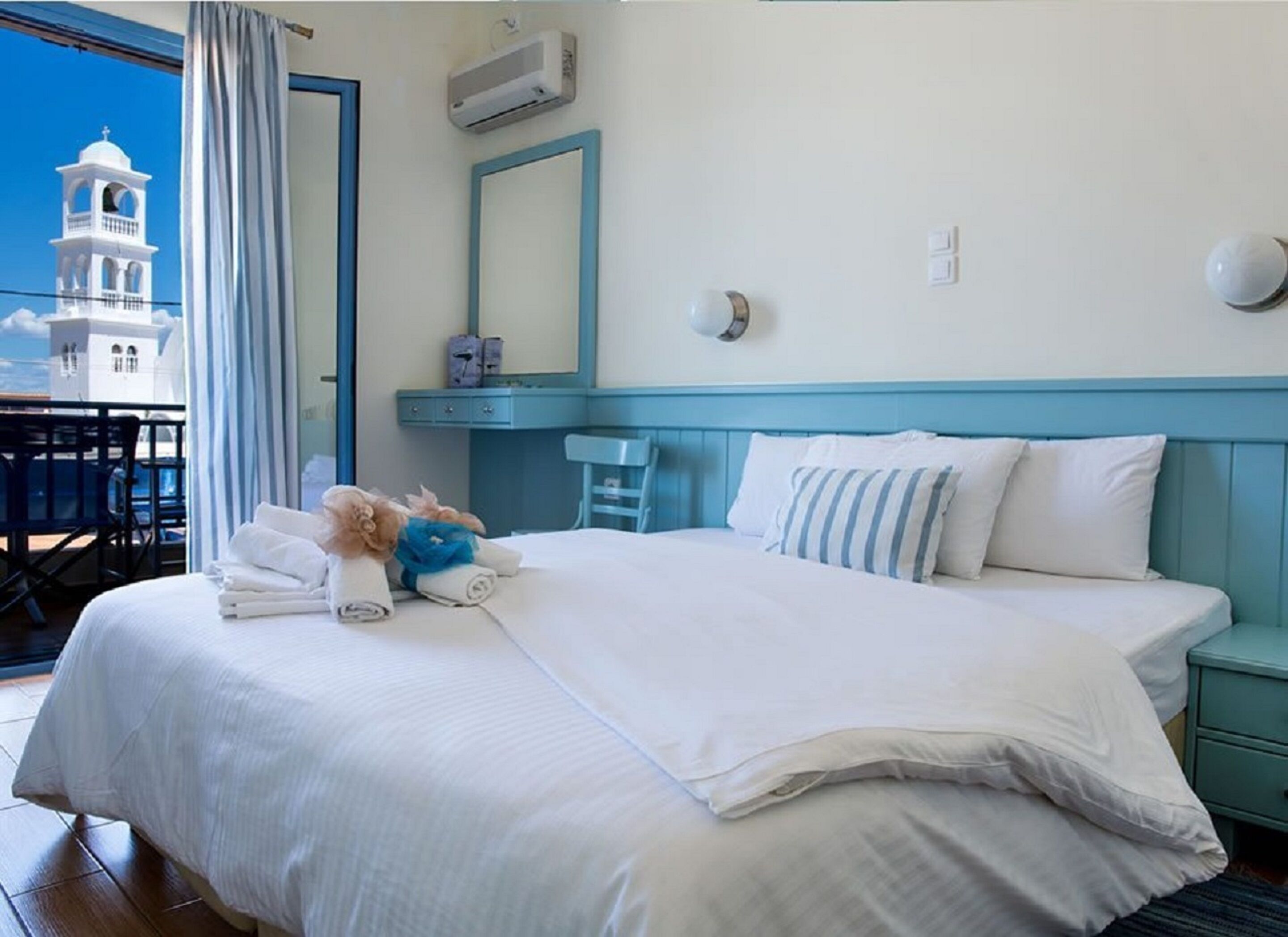 Et hotelværelse med en seng, et kommode, et spejl og udsigt til en hvid bygning med et tårn.