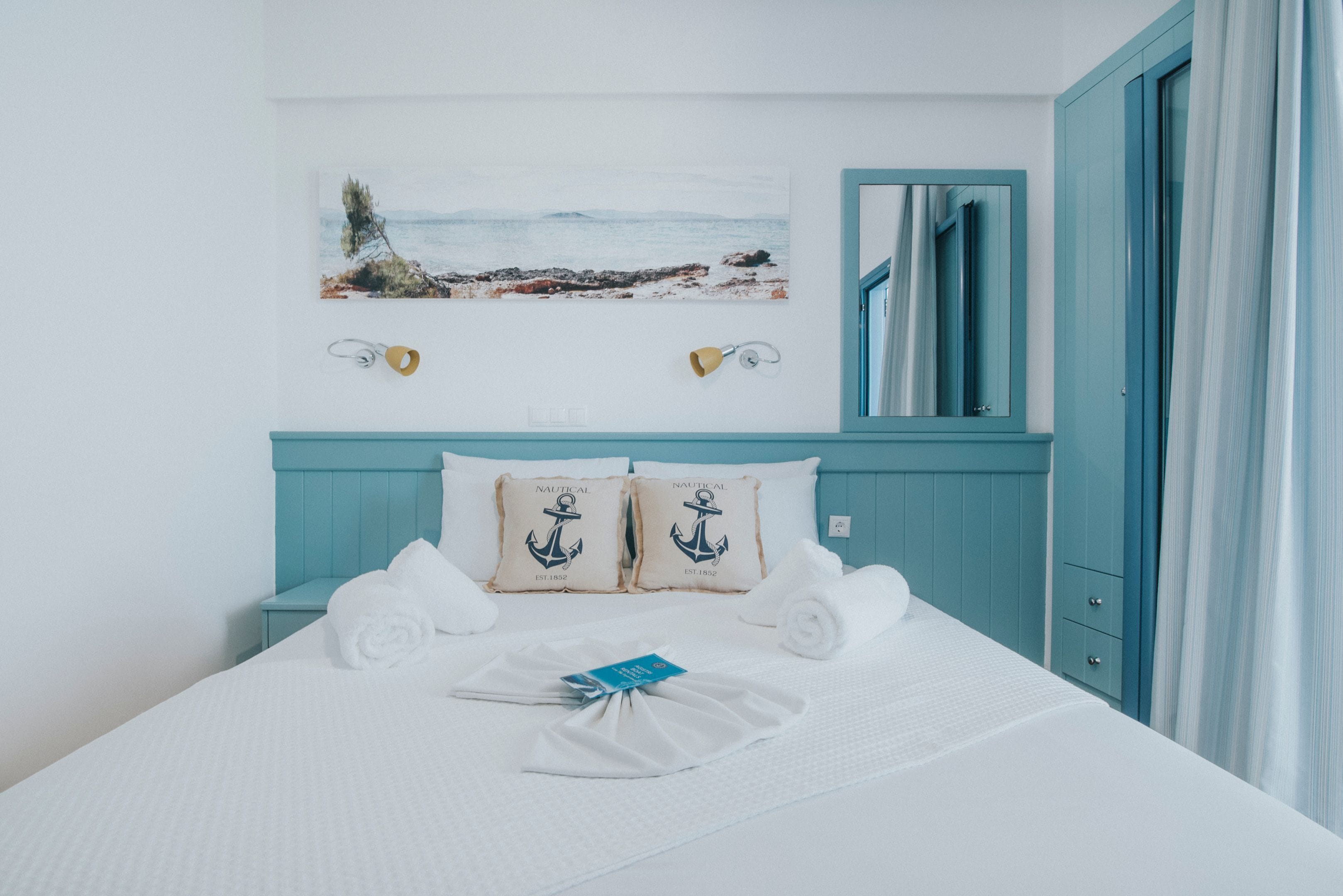 A neatly made bed with white linens, a nautical-themed pillow, and a folded towel.