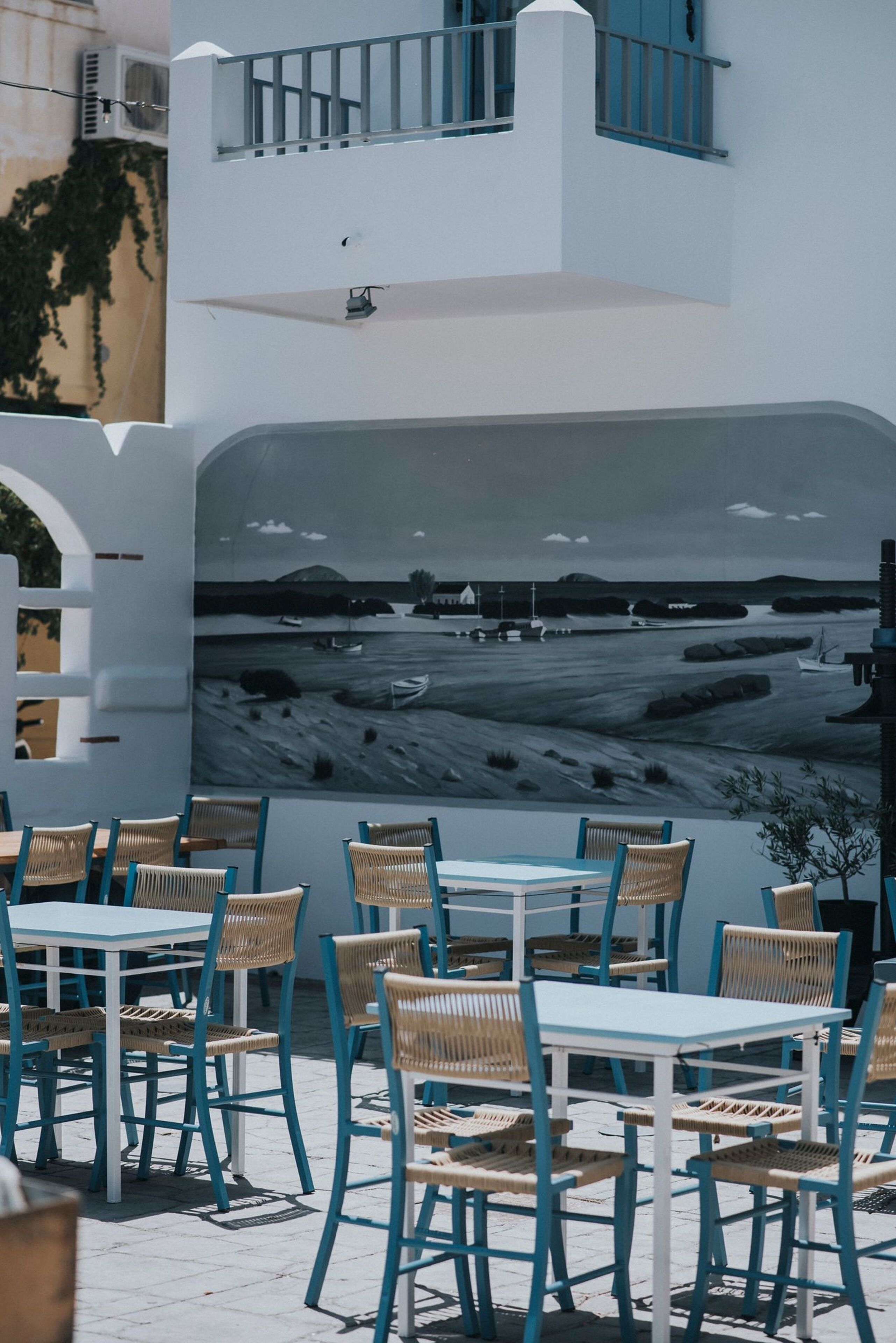 A seaside café with outdoor seating, white walls, and a mural of a coastal scene.