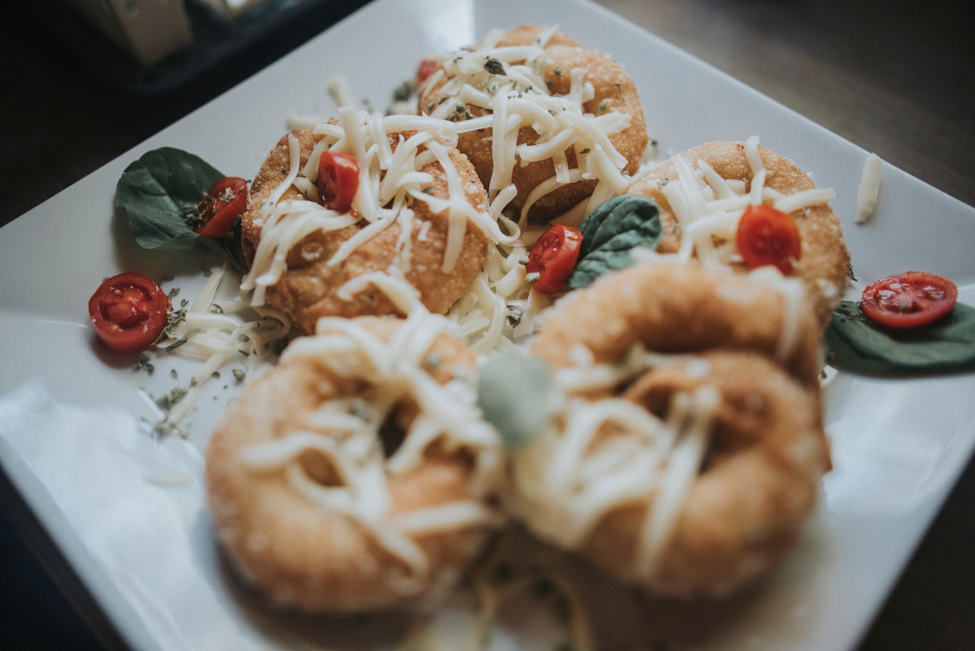 A plate of food with breaded items topped with cheese and garnished with tomatoes and basil.