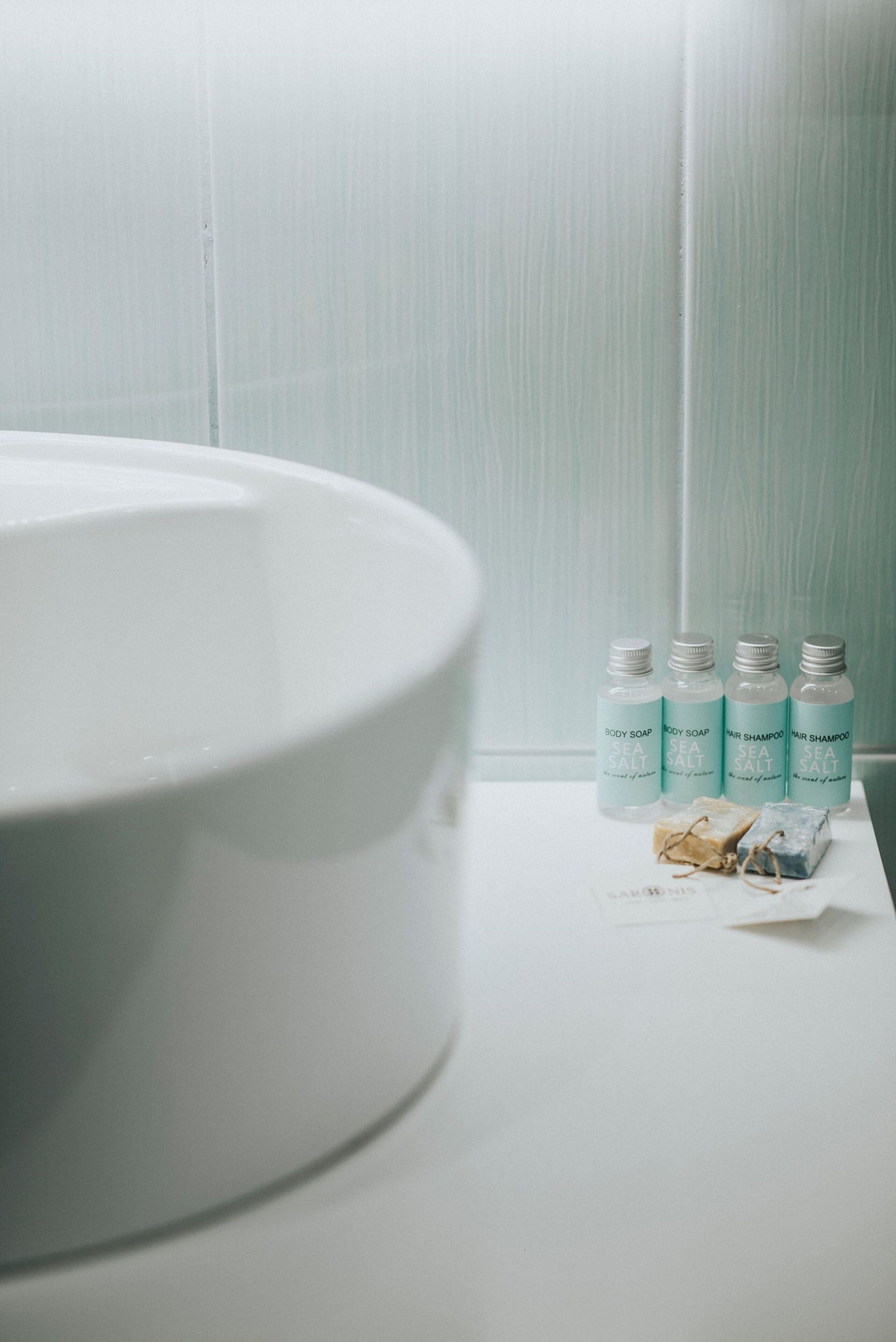 A bathroom with a white sink, four bottles of body soap, and two bars of soap on a white countertop.