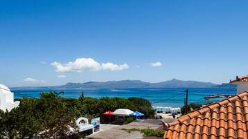 A coastal view with a clear blue sky, a beach, and a mountain range in the distance.