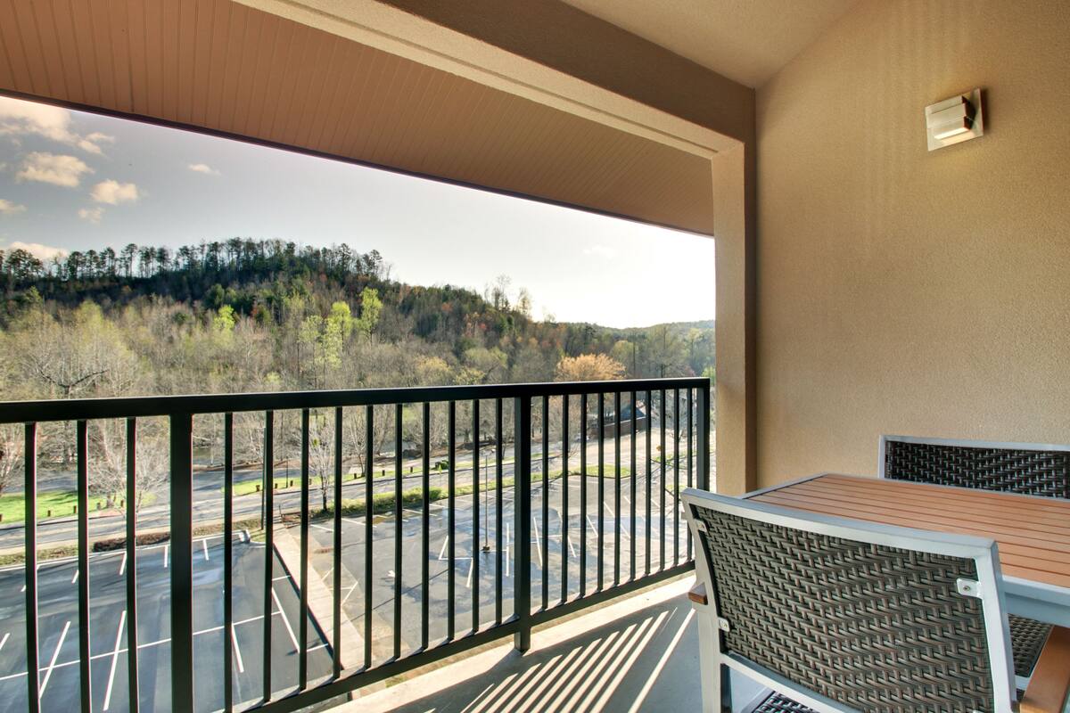 A balcony with a view of a parking lot and forested hills.