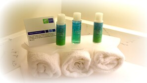 Een badkamer met drie flessen witte citrusshampoo, een witte handdoek en een kaartje met gratis toiletartikelen.