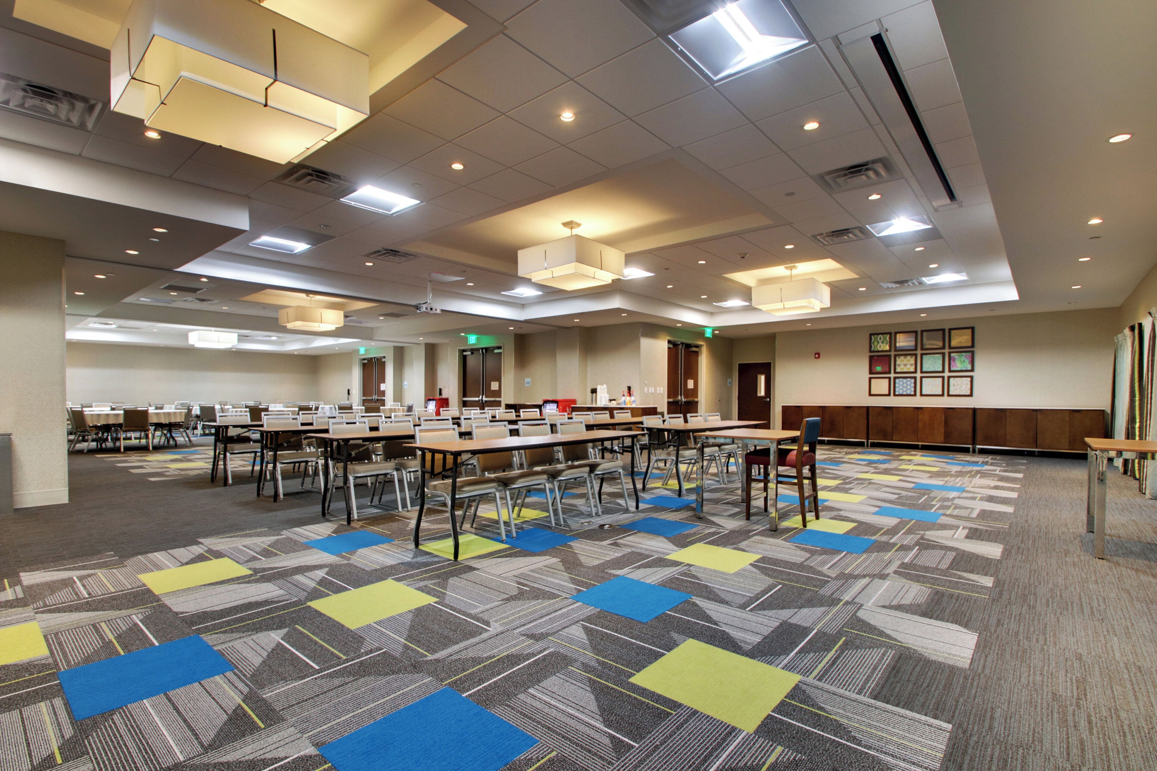 Un salón de conferencias con varias mesas y sillas, piso alfombrado e iluminación en el techo.