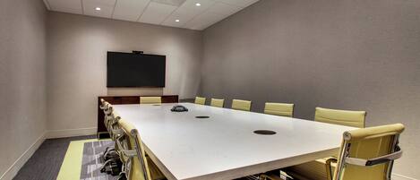 A conference room with a large table, chairs, a flat-screen TV, and a carpeted floor.