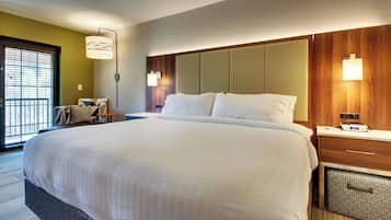 A hotel room with a large bed, a bedside table, a lamp, and a view of the outside through a window.