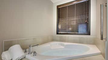 A bathroom with a large bathtub, a towel, and a window with blinds.