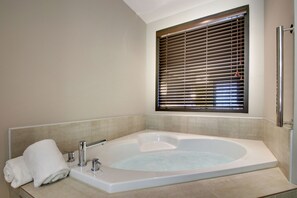 Een moderne badkamer met een groot bad, een handdoekhouder en een raam met zonwering.