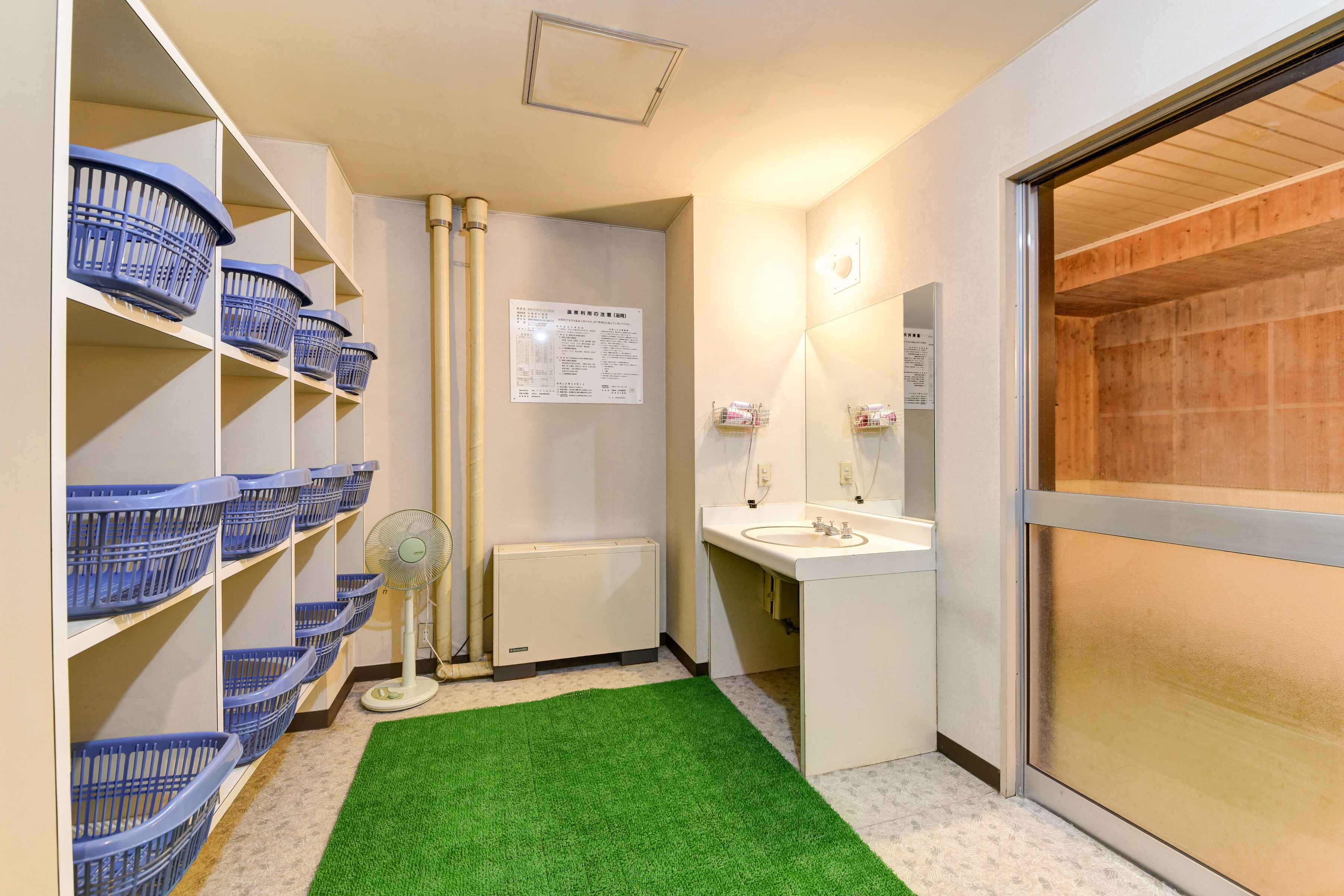 A bathroom with a green artificial grass floor, white cabinets, a sink, and blue baskets on shelves.