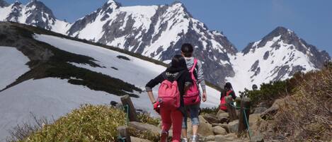 A group of hikers ascending a rocky mountain trail with snow-capped peaks in the background.