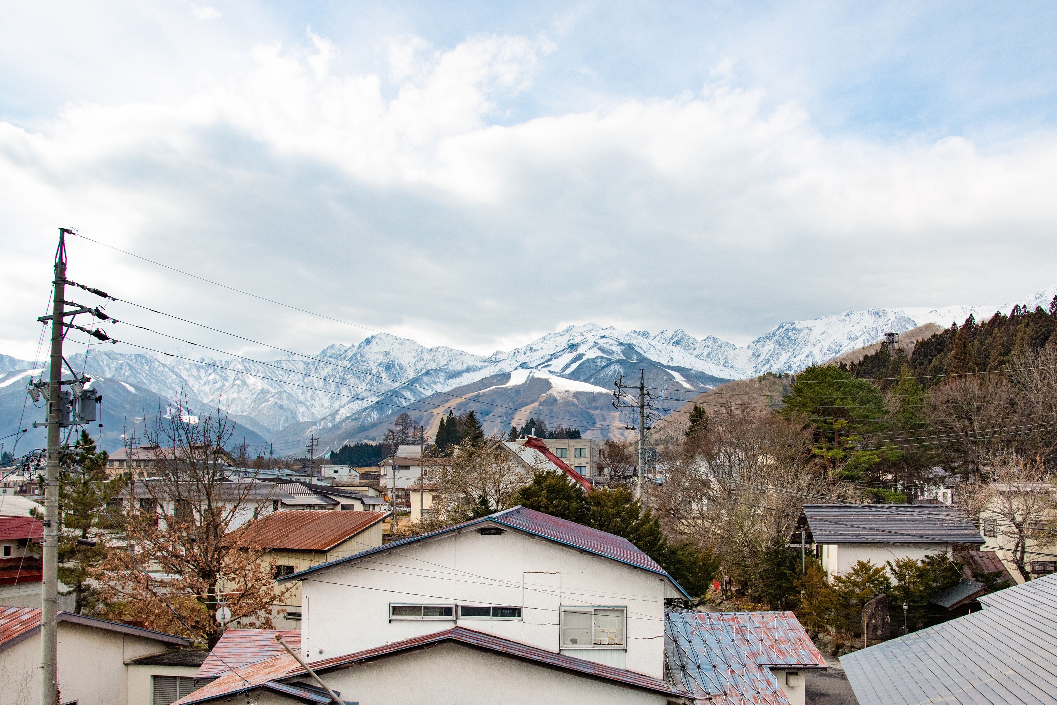 Un quartier résidentiel avec des maisons, une ligne électrique et, au loin, des montagnes enneigées.
