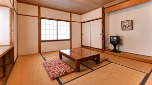 Een traditionele Japanse kamer met tatami vloerbedekking, een lage houten tafel en een televisie op een standaard.