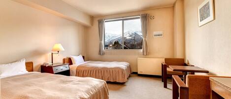 Habitación de hotel con dos camas, un escritorio, una silla, una lámpara, una ventana con vista a las montañas y un cuadro en la pared.
