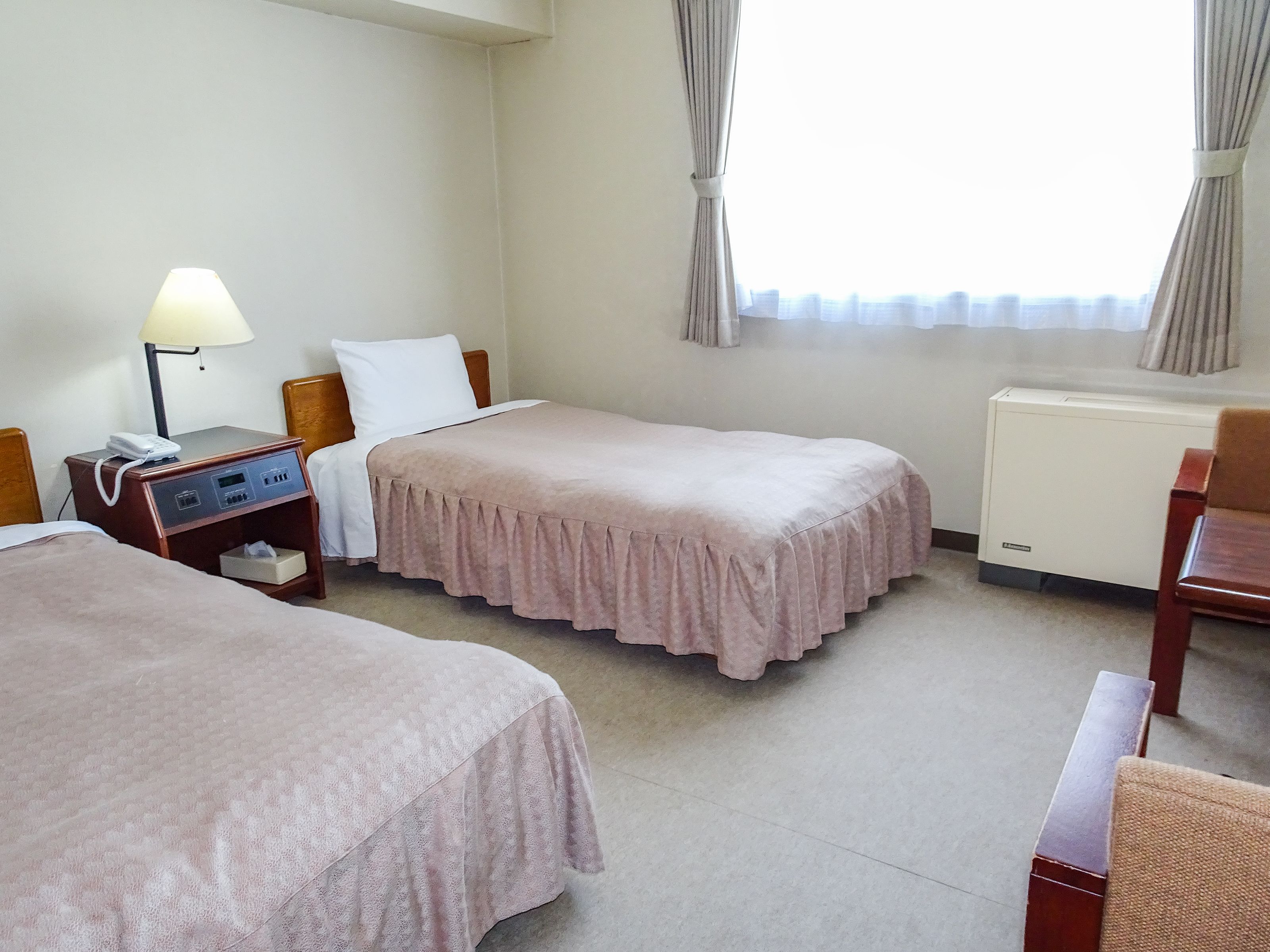 Een hotelkamer met twee enkele bedden, een nachtkastje met lamp, een stoel en een radiator.