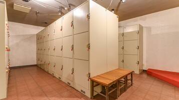 A locker room with multiple lockers, a wooden bench, and a tiled floor.