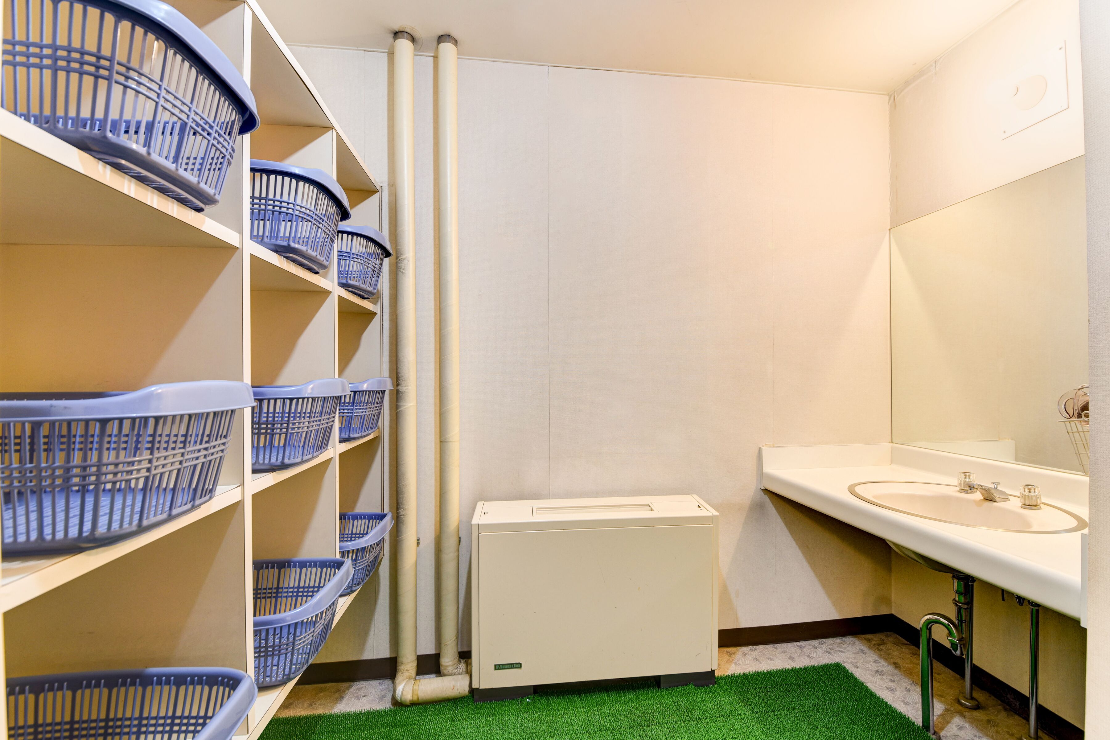 A bathroom with a white sink, a mirror, and a green artificial grass floor. There are blue baskets on shelves and a white radiator.
