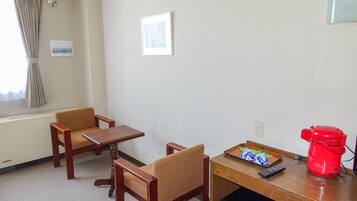A hotel room with two wooden chairs, a small table, a red kettle, and a refrigerator.
