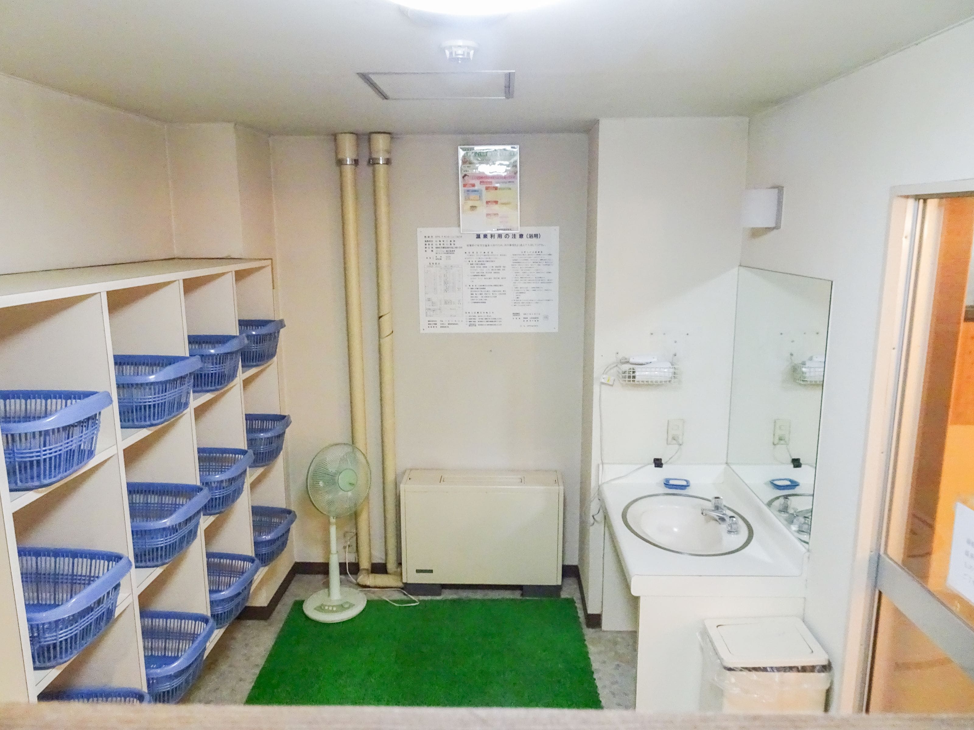 Une petite salle de bain propre, avec un lavabo blanc, un miroir, un tapis vert et des paniers bleus placés sur des étagères.