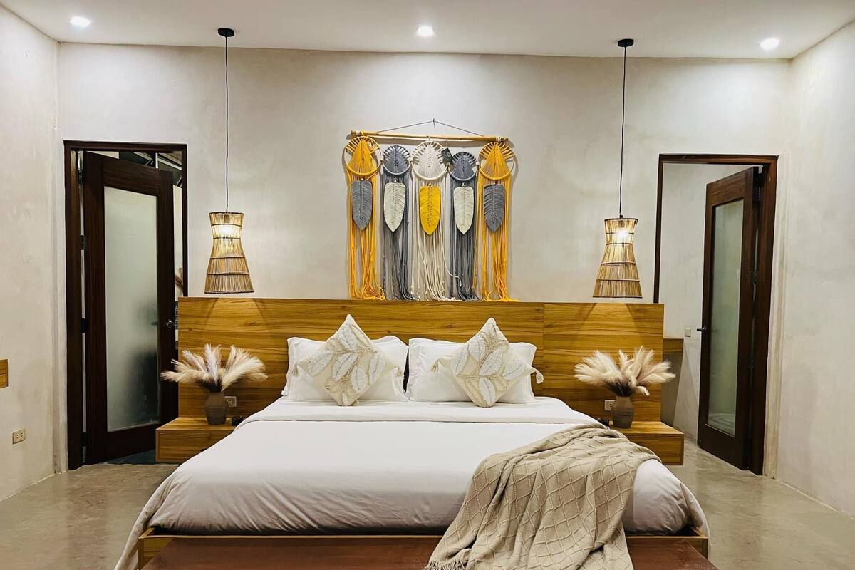 Ein modernes Schlafzimmer mit einem Holzkopfende, einem großen Bett mit weißer Bettwäsche, zwei Nachttischen mit Lampen und einer dekorativen Wanddekoration.