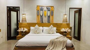 A modern bedroom with a wooden headboard, a large bed with white bedding, two bedside tables with lamps, and a decorative wall hanging.