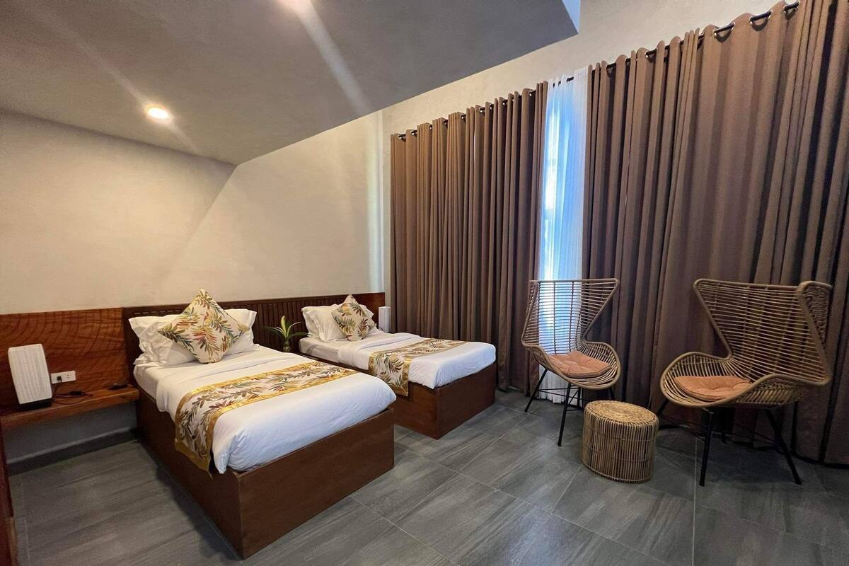 Ein Hotelzimmer mit zwei Betten, einer Sitzecke mit Sesseln und einem großen Fenster mit Vorhängen.