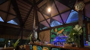 A bar area with a high ceiling and tropical mural. There are wooden tables and colorful chairs. - Lio Villas Resort (El Nido)