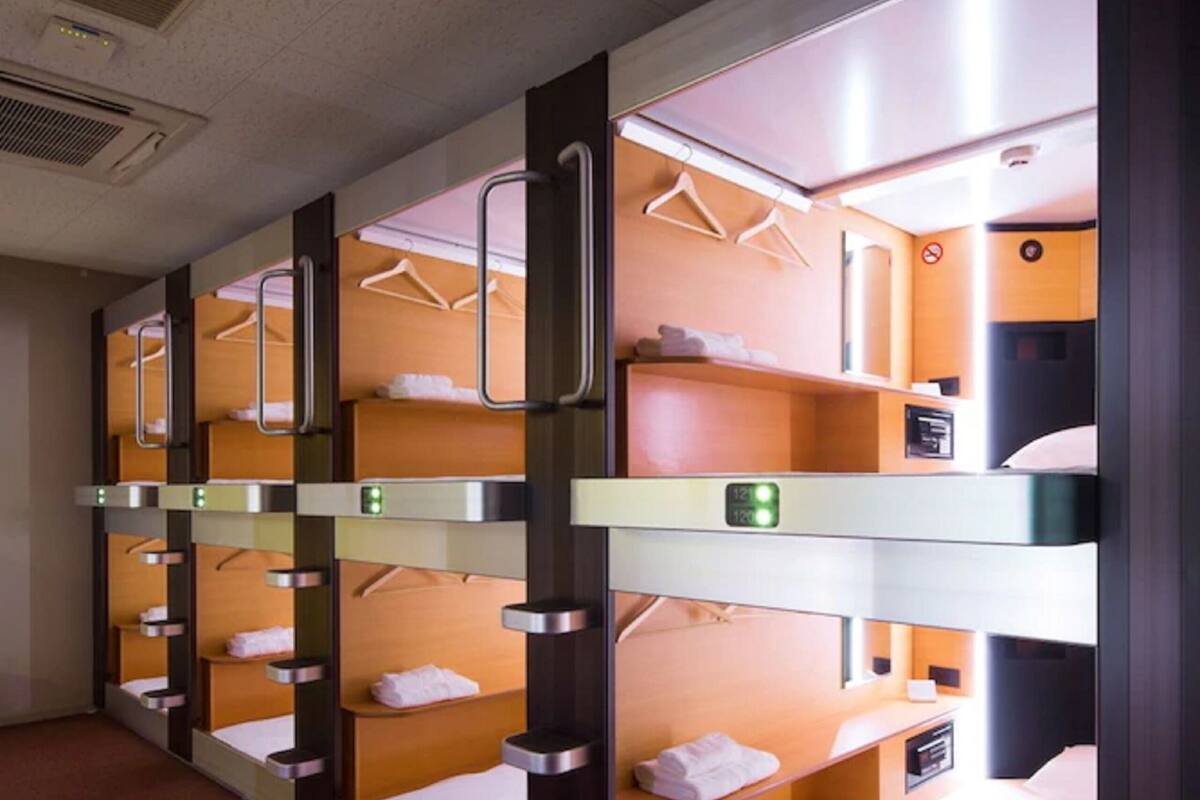 Une chambre d’hôtel avec des lits superposés, chacun étant doté d’une petite étagère et d’une tringle pour suspendre les vêtements.