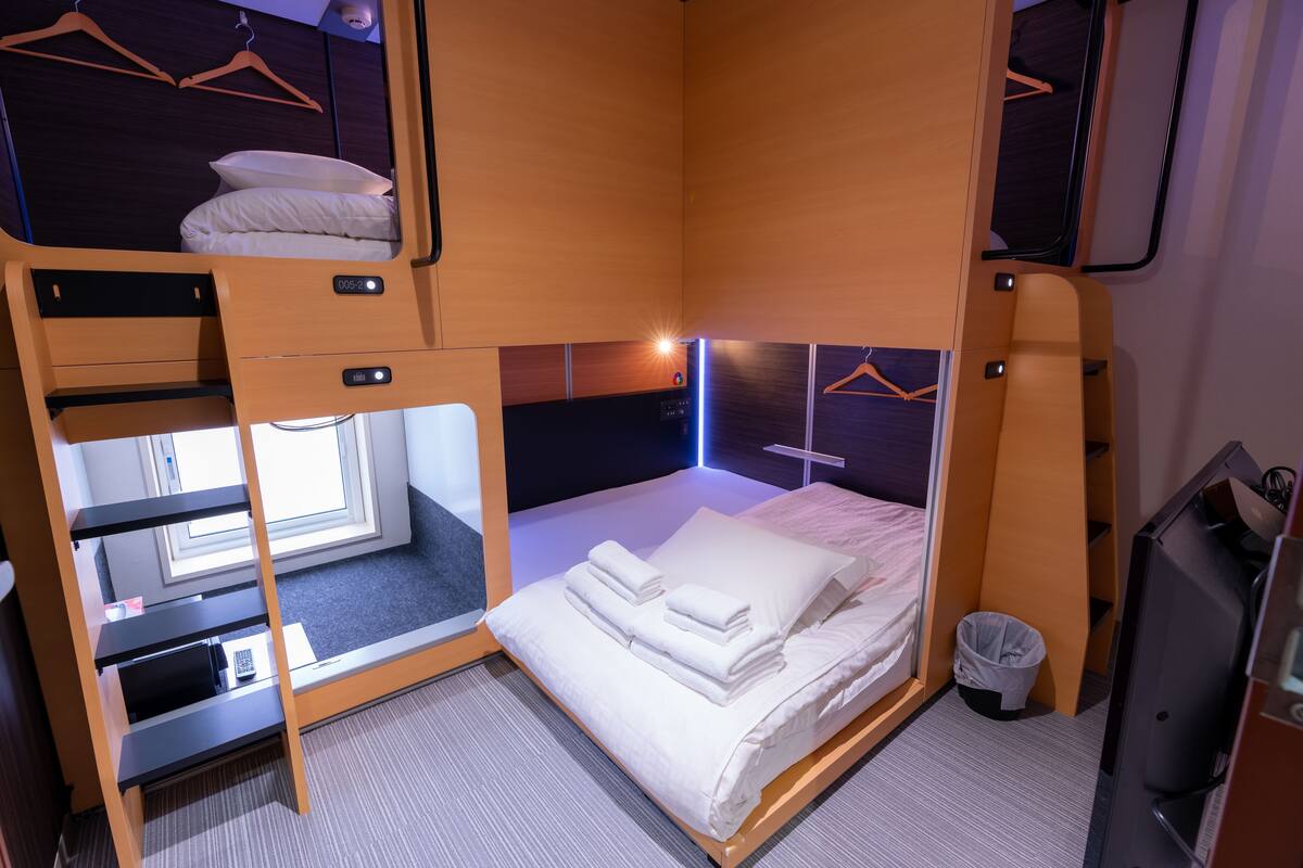 Une chambre d’hôtel compacte avec un lit superposé, un bureau avec un ordinateur portable, une télévision et une petite poubelle.