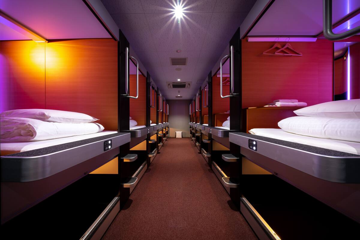 Une rangée de lits superposés dans une chambre d’hôtel, avec un couloir central.
