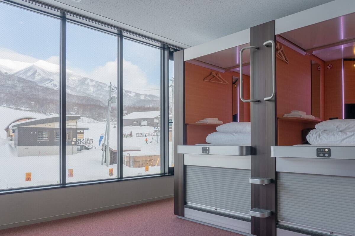 Une chambre d’hôtel avec de grandes fenêtres, un lit, une table de chevet et une vue sur une région montagneuse enneigée.