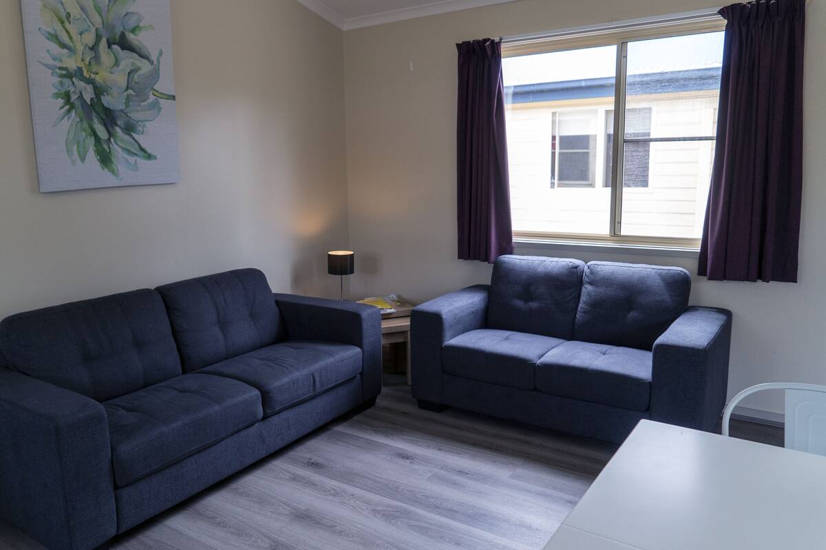 A room with two sofas, a small table, a lamp, and a painting on the wall.