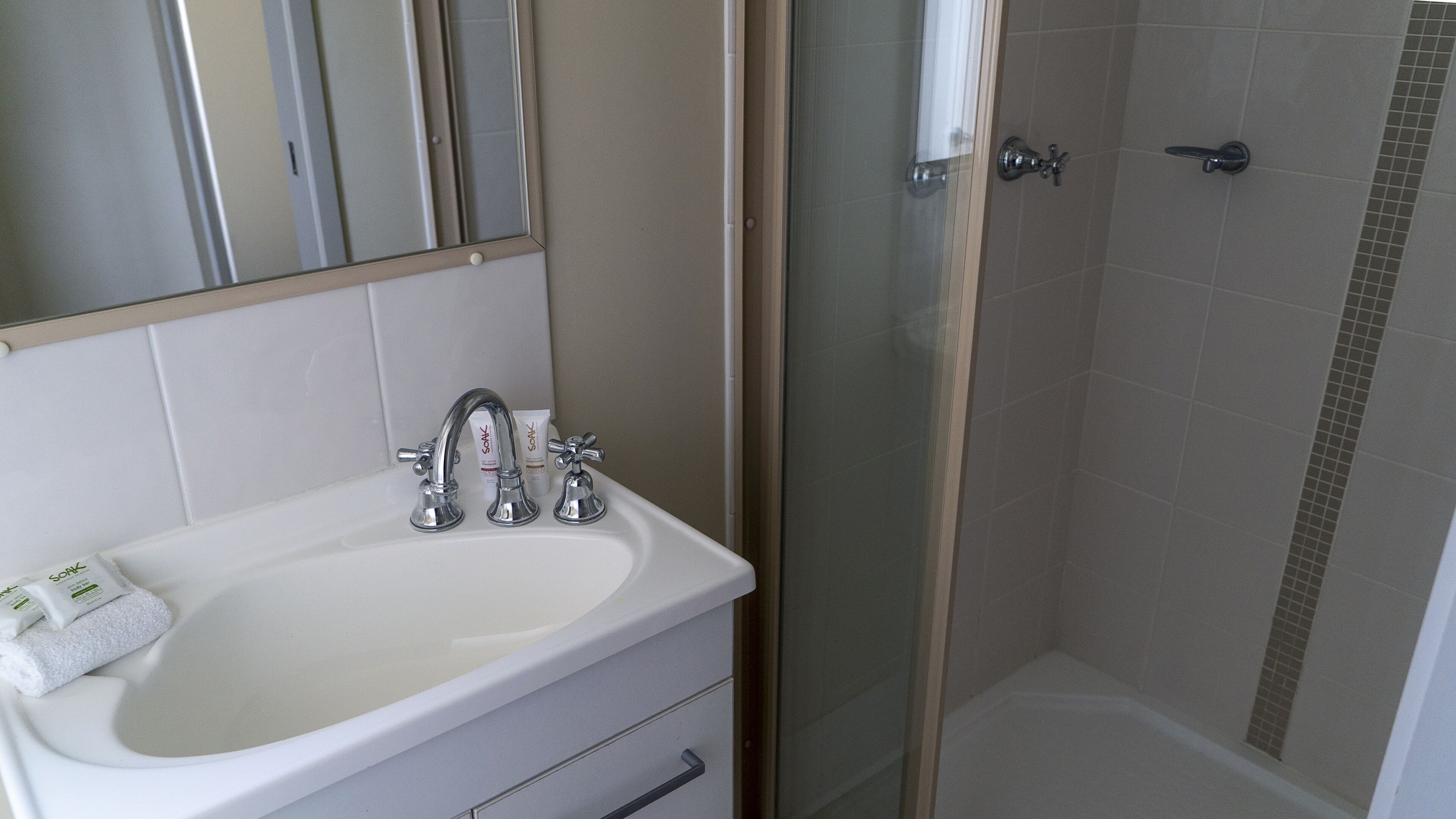 A bathroom with a white sink, two faucets, and a glass shower enclosure.