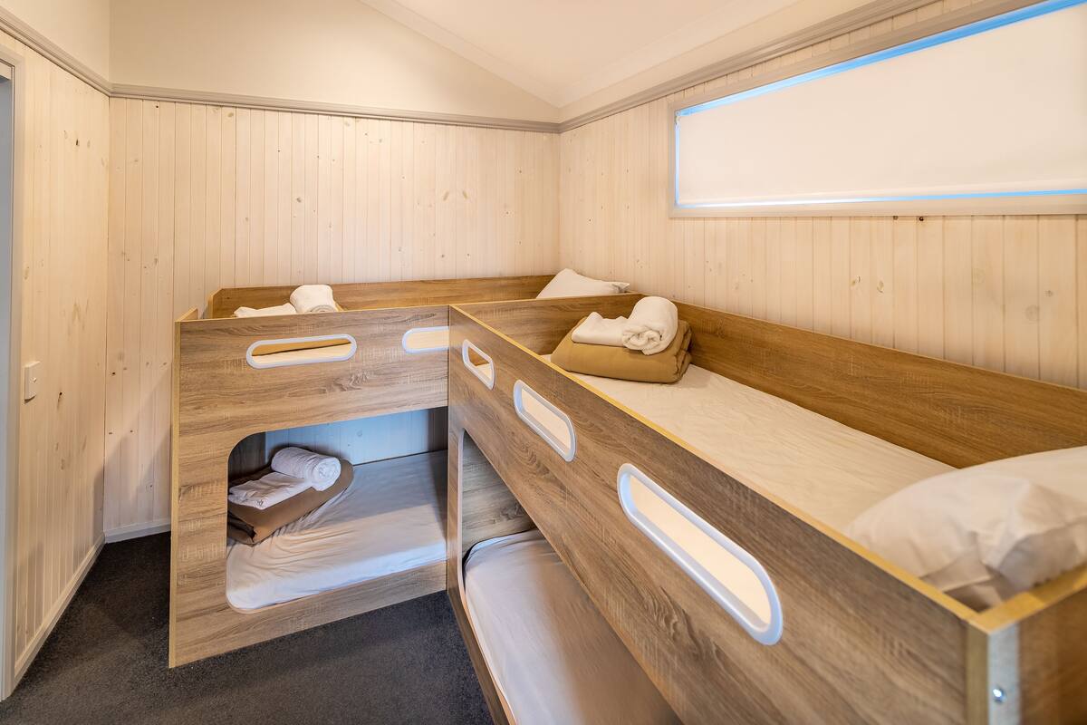 A compact room with bunk beds, wooden walls, and a window.