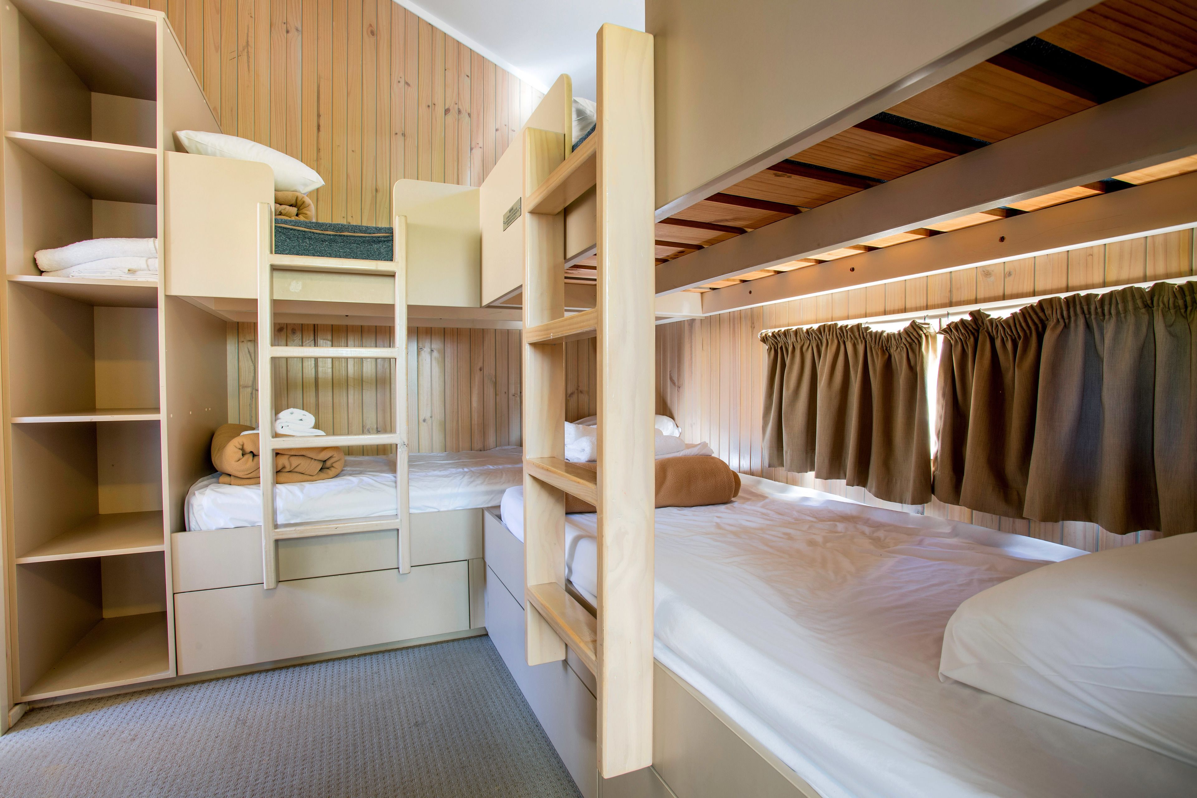 A bunk bed room with built-in shelving, a window with curtains, and a carpeted floor.