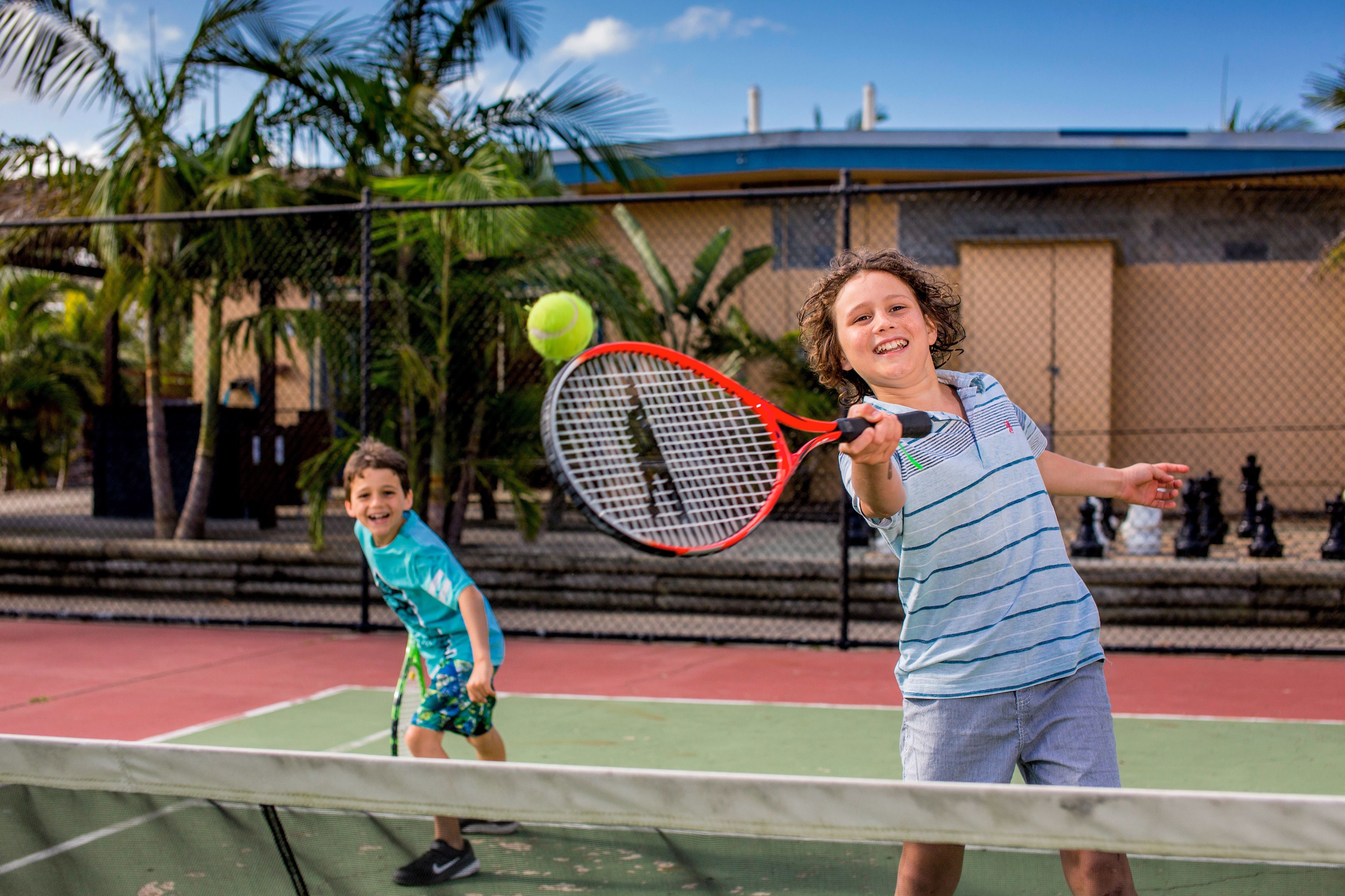 A tennis court with a net, palm trees, and a building in the background.