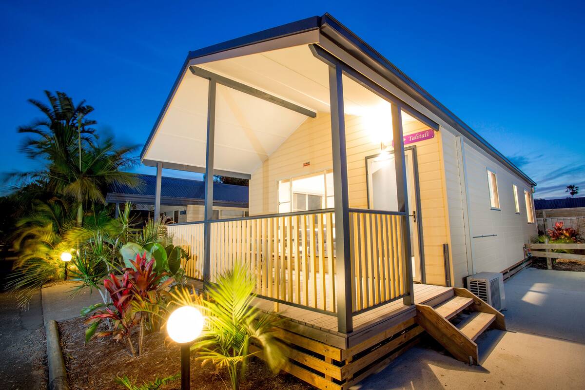 A wooden house with a covered porch, a staircase leading to the entrance, and a sign that reads "Tropicali".