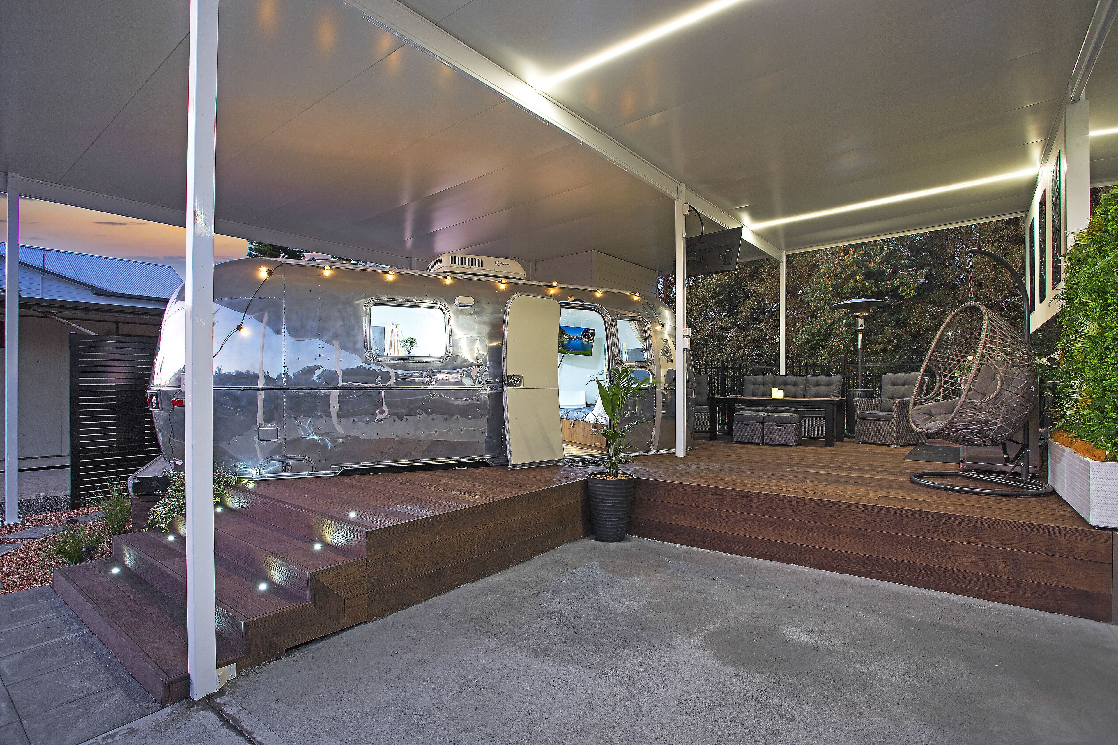 A covered outdoor area with a van, steps, seating, and a hanging chair.