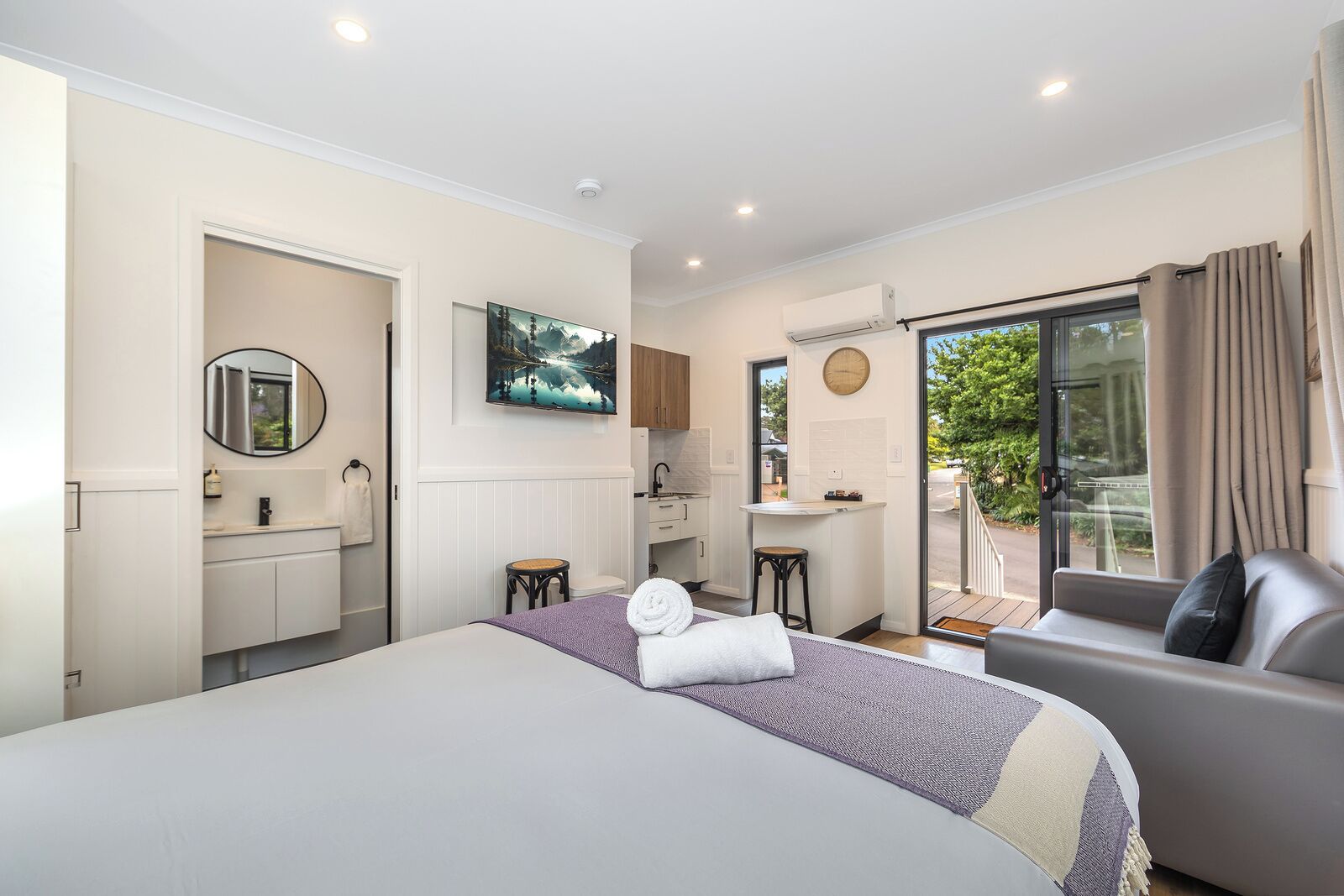 A bedroom with a bed, a desk, a chair, a bathroom, and a balcony with curtains.